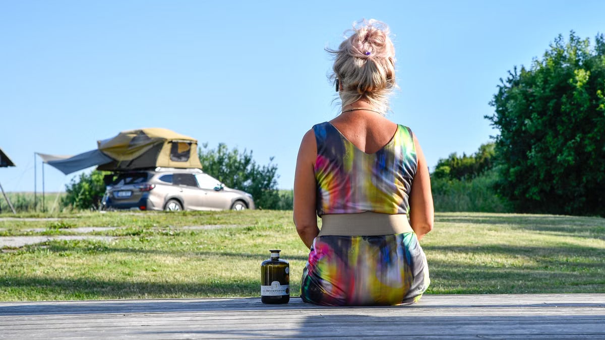 A woman in a colorful dress sits near a rooftop tent, enjoying a peaceful day outdoors in Simiste, Estonia.